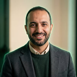 Portrait of Omar Hassan, a professional trader, smiling confidently against a warm cream background with a subtle forest gree